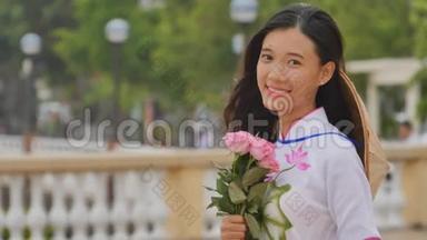 <strong>越南</strong>女孩穿着<strong>民族</strong>服装和服装，为相机摆姿势和微笑。 手里拿着粉红色